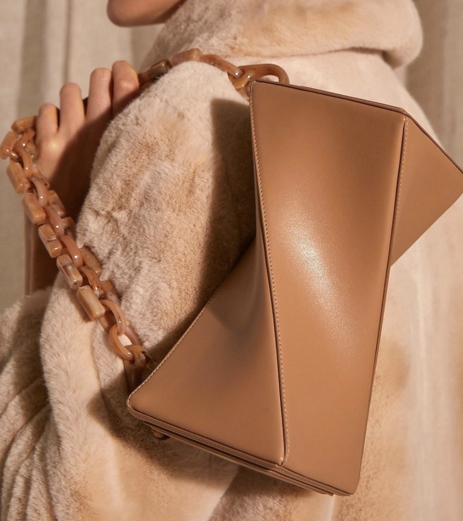 A woman wearing a fur coat holds a beige handbag over her shoulder